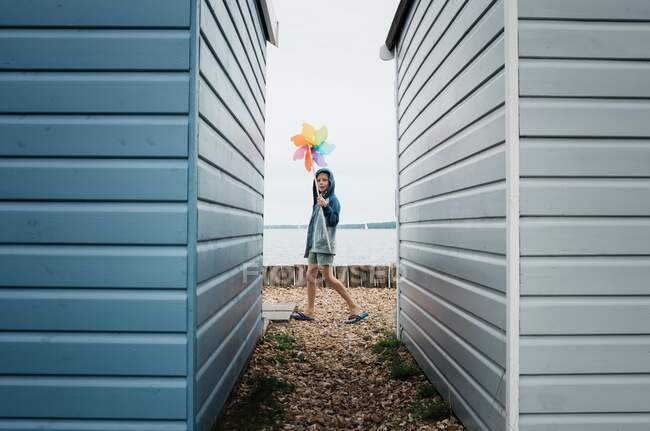 Девушка, идущая вдоль пляжа с ветряной мельницей рядом с пляжными хижинами — стоковое фото