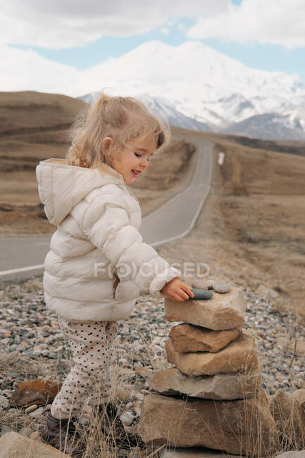 Una niña pequeña dobla una cairna de piedras cerca del Monte Elbrus - foto de stock