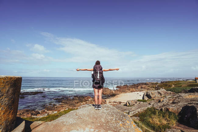 Peregrina con los brazos abiertos sobre una roca mirando al horizonte - foto de stock