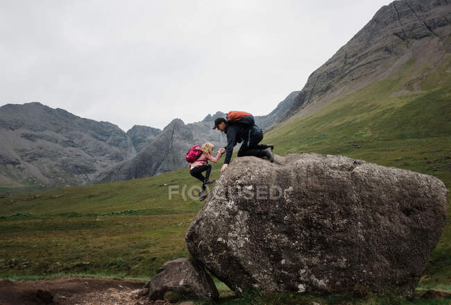Vater hilft seiner Tochter beim Klettern beim Wandern in den schottischen Highlands — Stockfoto