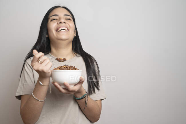 Портрет латиноамериканки середнього віку сміється під час їжі чаші граноли з сірим тлом . — стокове фото