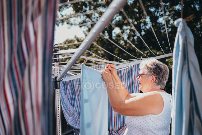 Старшая женщина вешает белье на открытую бельевую веревку. — стоковое фото