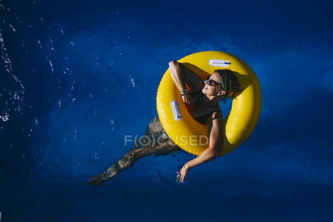 66-річна жінка насолоджується сонячним днем у басейні з жовтим поплавцем — стокове фото
