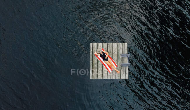 Aerial of woman relaxing alone on floating dock on lake in summer. — Stock Photo
