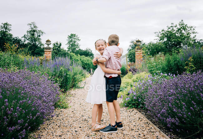 Mädchen und Junge umarmen und lachen in einem schönen Blumenfeld — Stockfoto