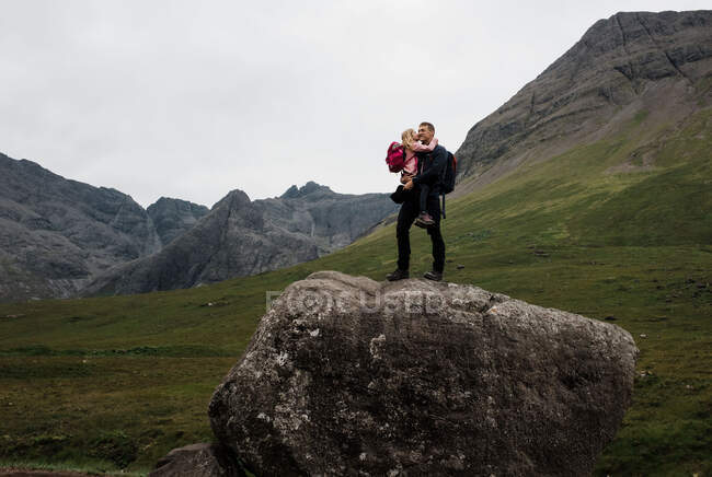 Батько обіймає свою дочку після того, як виліз на гігантський валун у Шотландії. — стокове фото