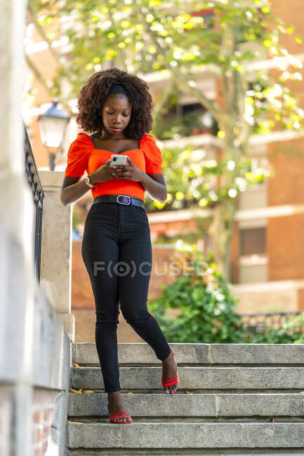 Hermosa fotografía de una joven africana caminando y enviando un mensaje desde su teléfono inteligente - foto de stock