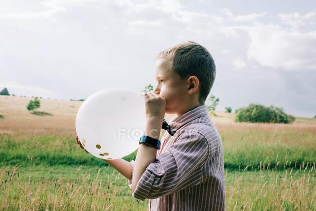 Smartly dressed boy blowing up a balloon at a wedding in summer — Stock Photo