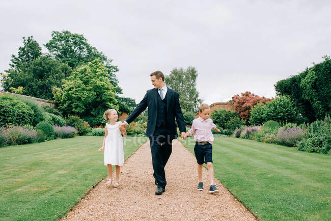 Pai e filhos em um casamento caminhando através do campo de flores — Fotografia de Stock