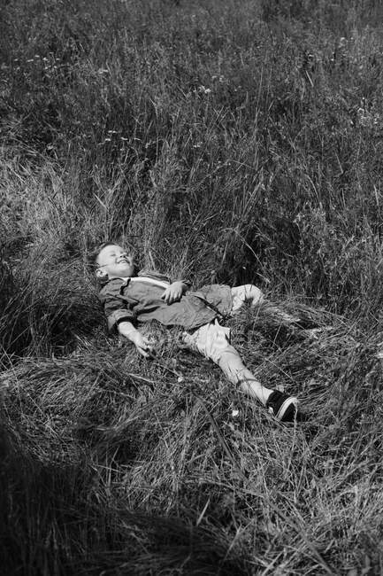 Щасливий хлопчик лежить на траві в літньому парку. Мила позитивна дитина — стокове фото