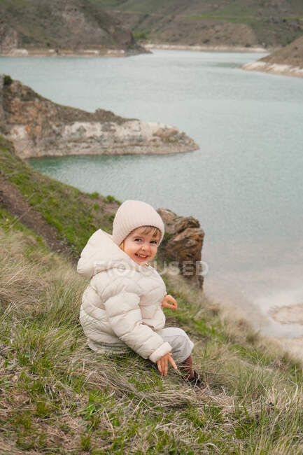 Kleines Mädchen drehte sich um, um in die Kamera zu schauen. Sitzen auf dem See — Stockfoto