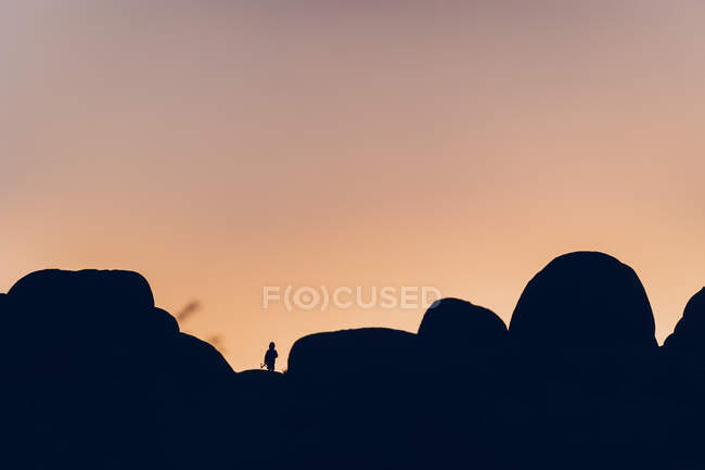Силует хлопчика серед каменів на заході сонця — стокове фото
