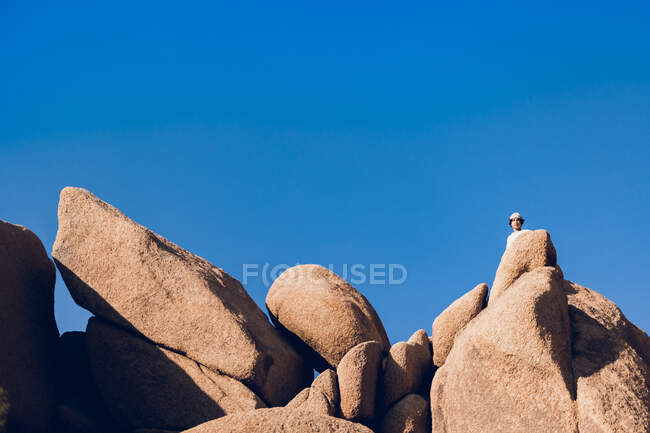 Adolescente escondido detrás de grandes rocas en el desierto. - foto de stock