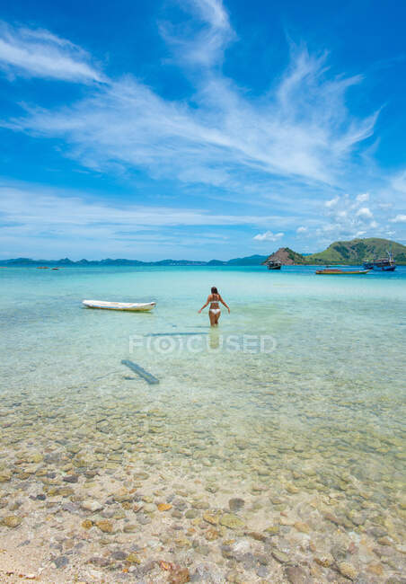 Chica en el paraíso camina hacia la canoa blanca fuera de la isla de Indonesia - foto de stock