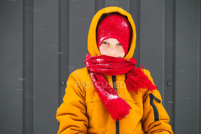 Boy in warm jacket and hat standing and looking in front of camera — Stock Photo