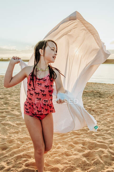 Счастливая молодая девушка использует простыню как плащ на озере — стоковое фото