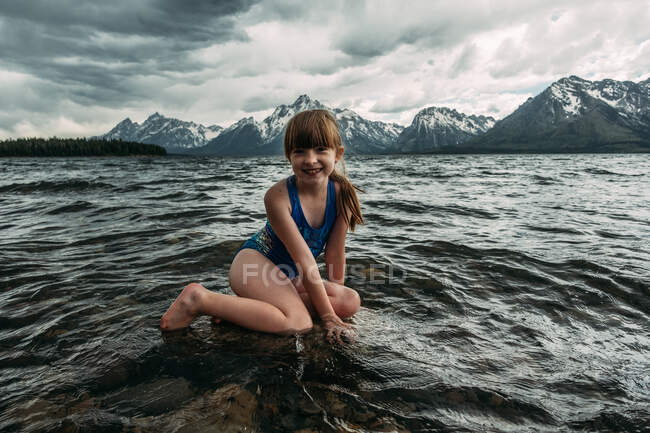 Young girl sitting in mountain lake on a cloudy day — Stock Photo