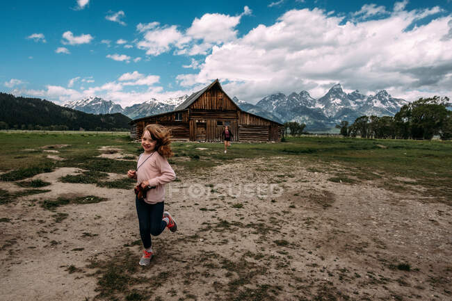 Giovani ragazze che corrono fuori da un vecchio fienile vicino a una catena montuosa epica — Foto stock
