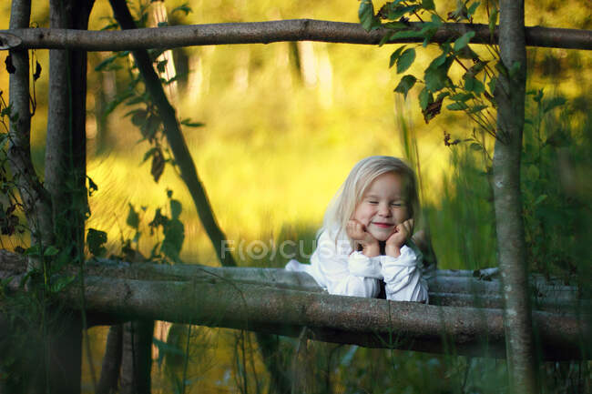 Porträt eines Mädchens, das auf Baumstämmen liegt und ihr Gesicht mit den Händen stützt. — Stockfoto