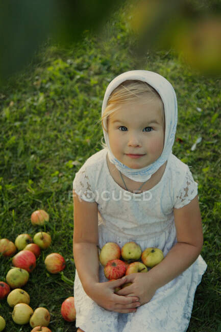 La chica se sienta en la hierba y sostiene manzanas en sus manos. - foto de stock