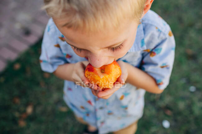 Close up shot of Caucasian boy eating peach in front yard — Stock Photo