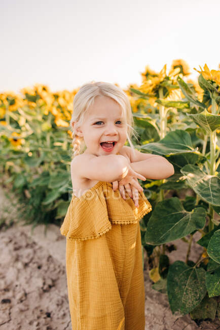 Zweijähriges kaukasisches Mädchen lacht beim Spielen in Sonnenblumen — Stockfoto