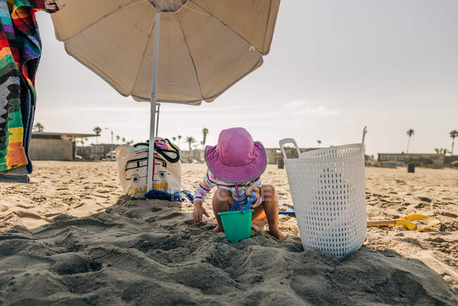 Toddler girl plays under umbrella in sand at Ocean Beach — Stock Photo