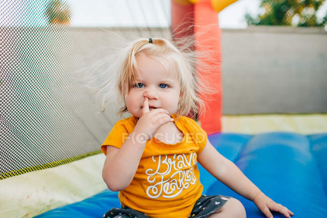 Blonde toddler girl picks nose while playing on jump house in backyard — Stock Photo