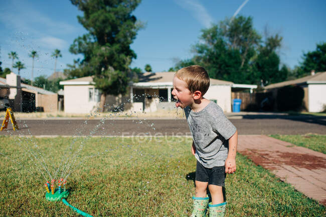 White little boy swallows sprinkler water on hot sunny day — Stock Photo