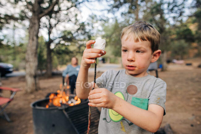 Four year old boy puts marshmallow on stick by campfire — Stock Photo