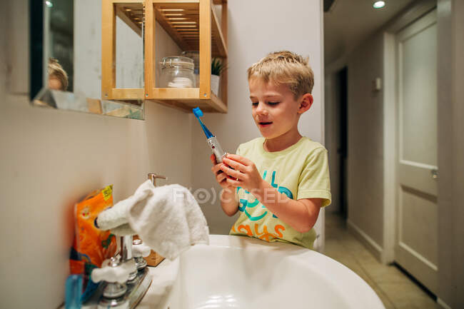 Jeune garçon se brosse heureusement les dents avec une brosse à dents électrique — Photo de stock