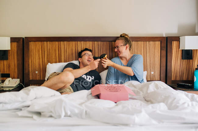 Os pais comem donuts na cama enquanto desfrutam da estadia no hotel — Fotografia de Stock