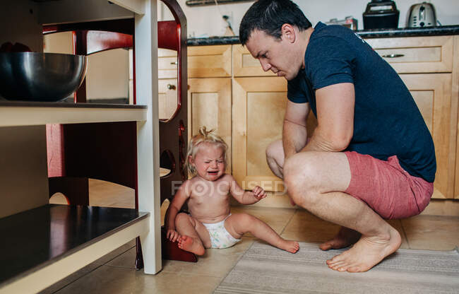 Dad looks down at diapered toddler girl while crying in kitchen — Stock Photo