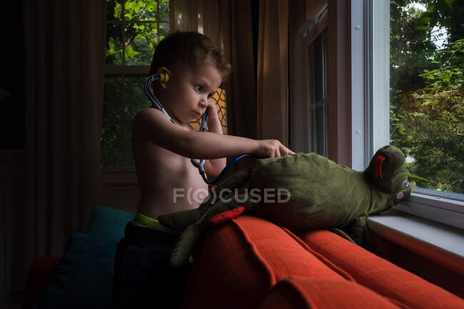 Toddler listens to a stuffed dragon's heart with a toy stethoscope — Stock Photo