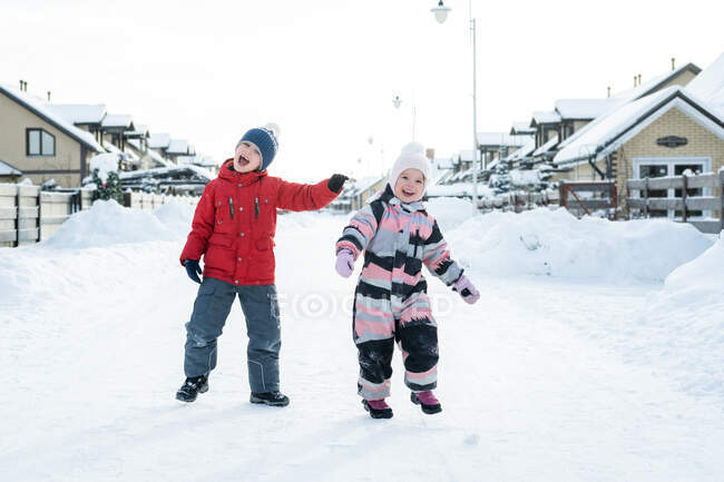 Duas crianças se divertem andando na aldeia de inverno. — Fotografia de Stock