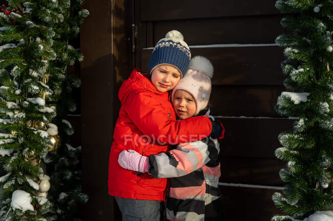 Dos niños, hermano y hermana, abrazándose en el pueblo de invierno. - foto de stock