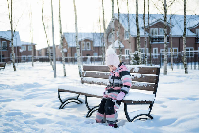 Das süße Mädchen sitzt auf einer Bank im Winterdorf. — Stockfoto