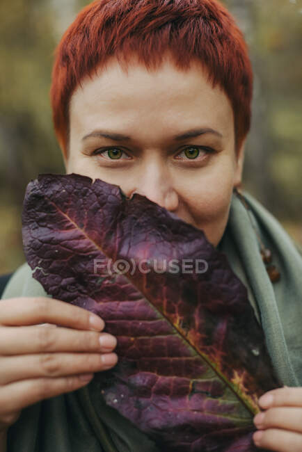 A middle-aged woman of 30-40 years old with an autumn burgundy leaf, her face is covered. Closeup portrait, young adult woman — Stock Photo