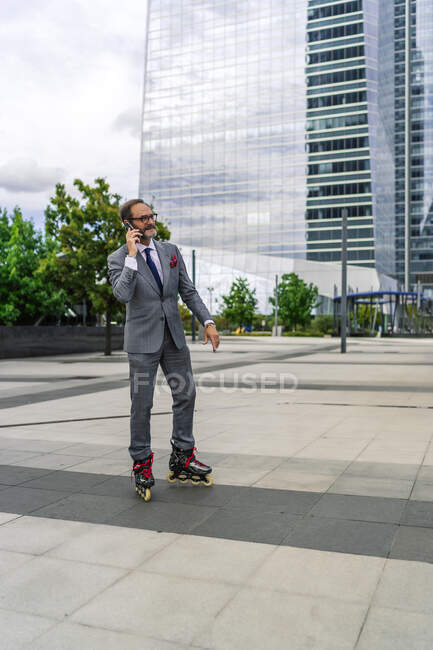 Patinaje ejecutivo con sus patines en línea mientras habla en su teléfono inteligente - foto de stock