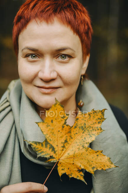 A middle-aged woman of 30-40 years old with an autumn maple leaf in her hand. Positive portrait close-up, female young adult — Stock Photo