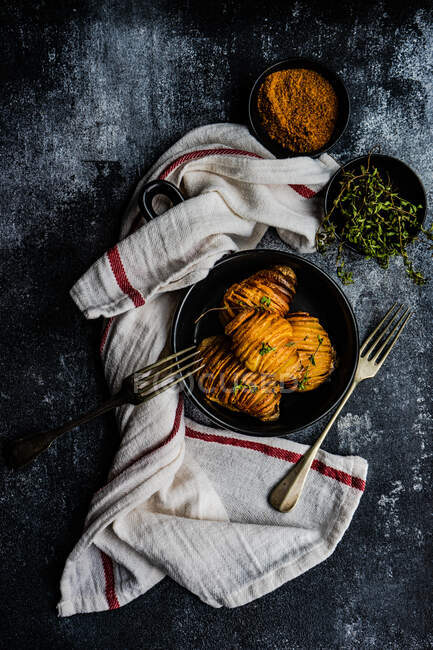 Pommes de terre Hasselback cuites au four avec des herbes fraîches et des épices servies dans un bol sur fond de béton — Photo de stock