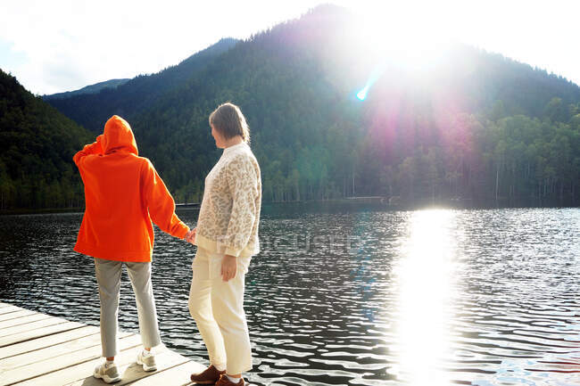 Filha e mãe caminham em um convés de madeira em lagos quentes — Fotografia de Stock