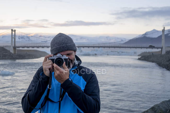 Um homem tirando uma foto com uma paisagem nevada no fundo na Islândia — Fotografia de Stock