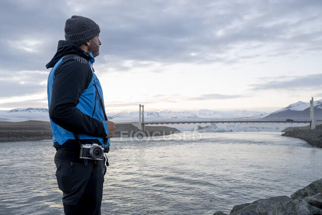 A man holding a photo camera over his shoulder with a snowy landscape in the background — Stock Photo