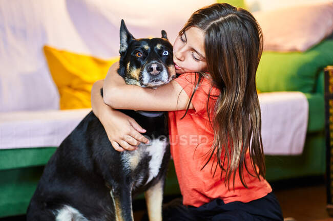 Маленькая девочка обнимает собаку, развлекаясь дома. — стоковое фото