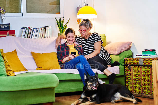 Una pareja lesbiana acostada en el sofá con su perro mascota. - foto de stock