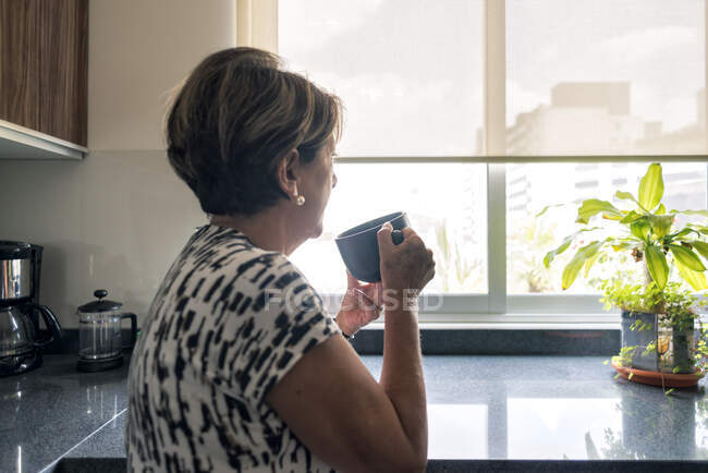 Молода жінка п'є каву на кухні — стокове фото