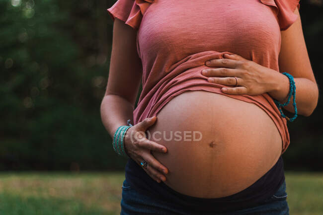 Беременная женщина держит живот на траве в парке. — стоковое фото