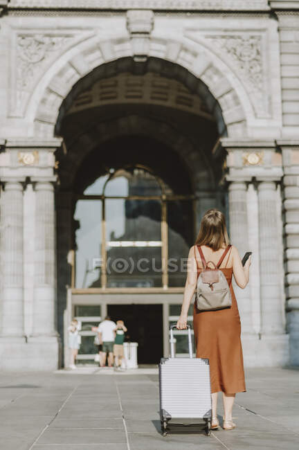 Молодая женщина с чемоданом гуляет по городу — стоковое фото