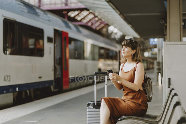 Jovem mulher com mochila sentada na plataforma ferroviária — Fotografia de Stock